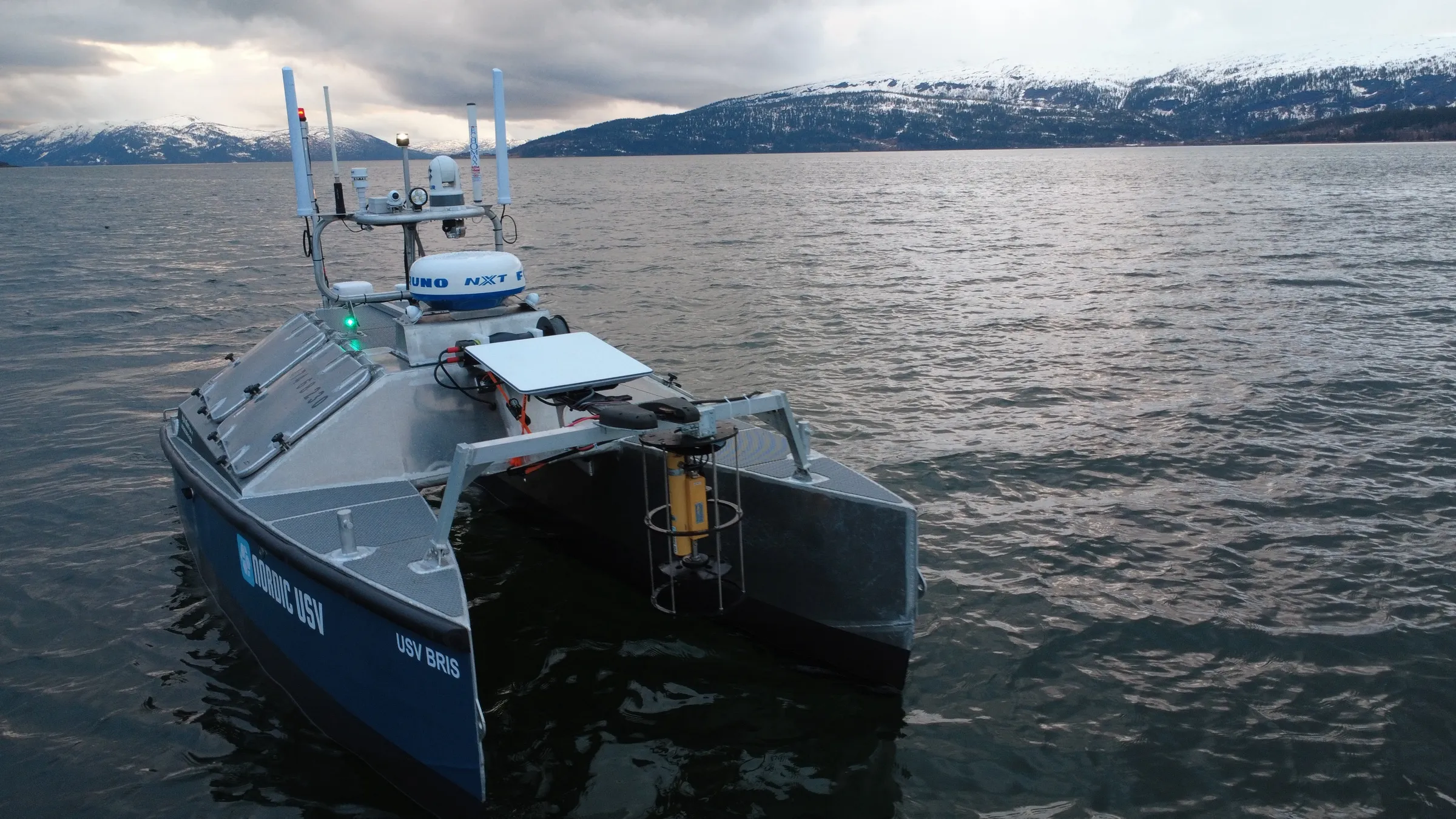 USV Bris med CTD-sensor i fjorden, med snødekte fjell i bakgrunnen.